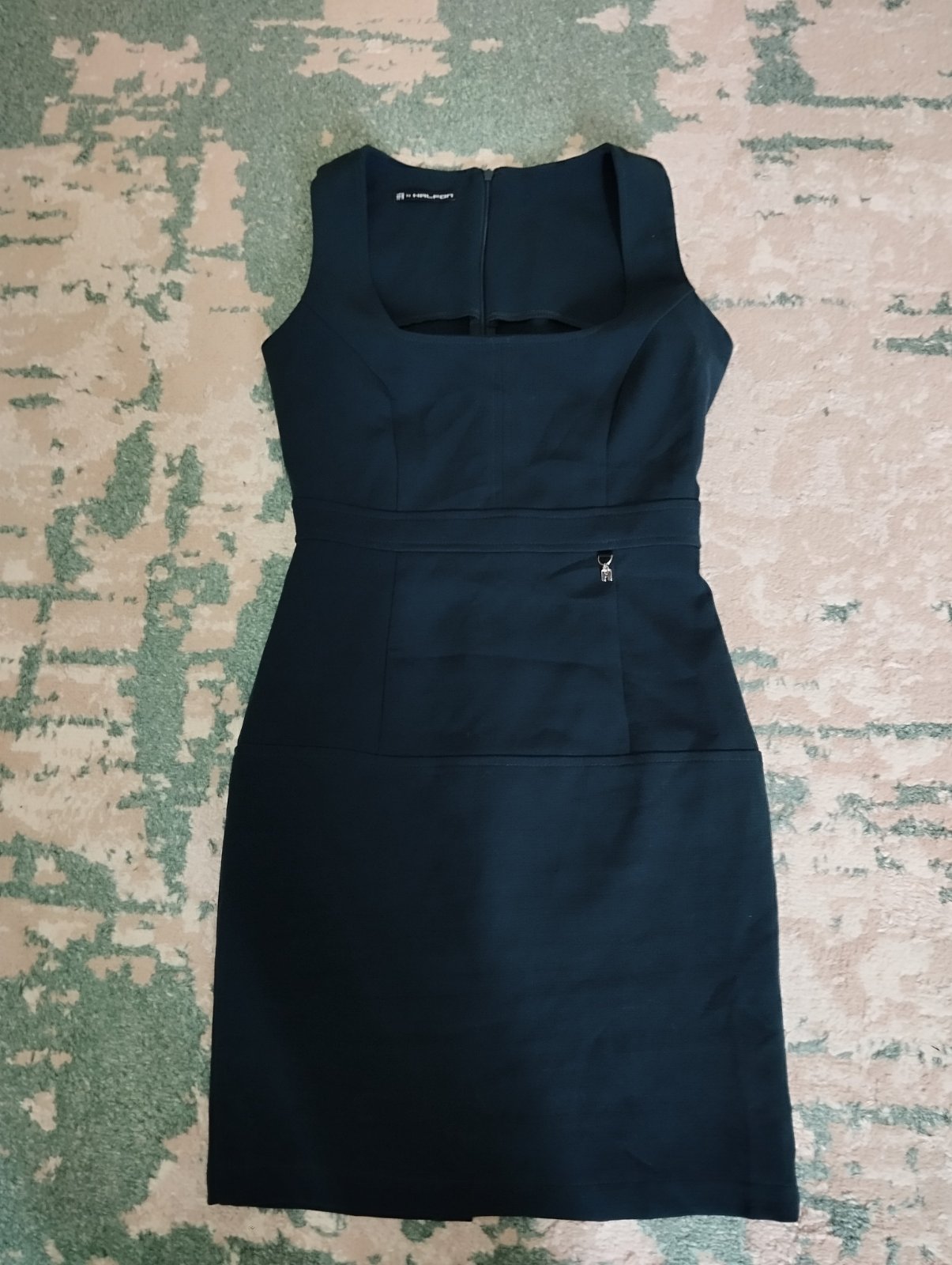 Robe fourreau sans manches vert foncé avec un décolleté carré, un détail de ceinture et une petite breloque dorée sur le devant