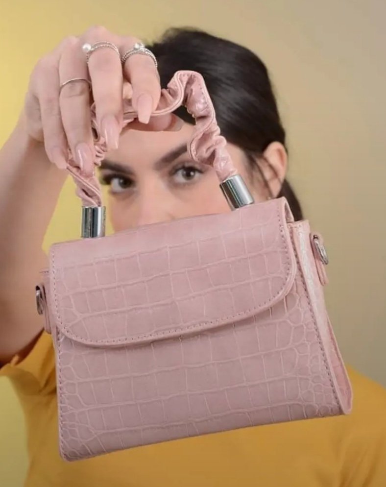 Ce produit est un petit sac à main rose avec une texture effet crocodile et une poignée froncée