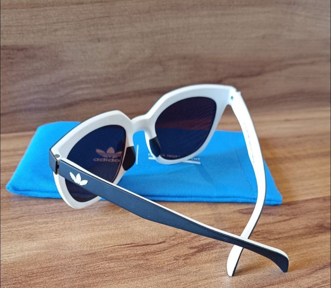 Il s'agit de lunettes de soleil Adidas Originals modèle OR0106 21A avec monture blanche et verres fumés, accompagnées de leur étui et chiffonnette. 