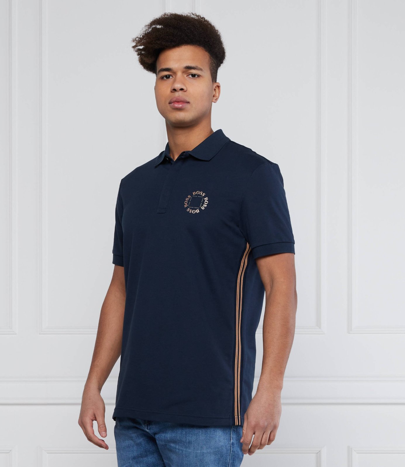 Ce polo est un modèle bleu marine de la marque BOSS avec un logo circulaire distinctif sur la poitrine et des bandes contrastées sur les côtés.