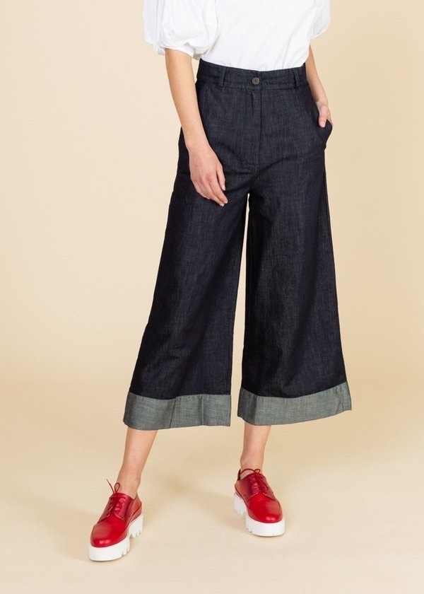 Pantalon large en denim bleu foncé, style cropped/capri à jambes évasées, avec taille haute et plis discrets à l’avant