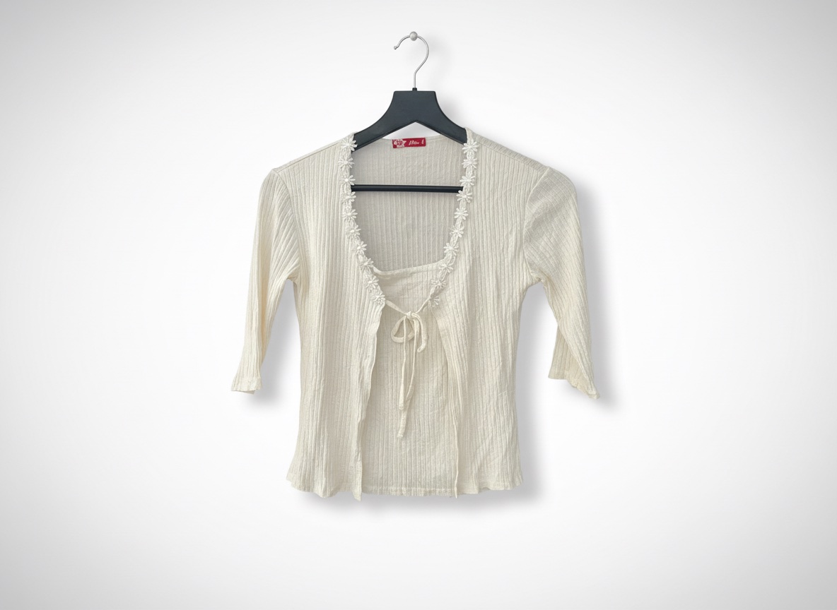 A white cardigan features a ribbed texture and delicate daisy lace trim along the neckline
