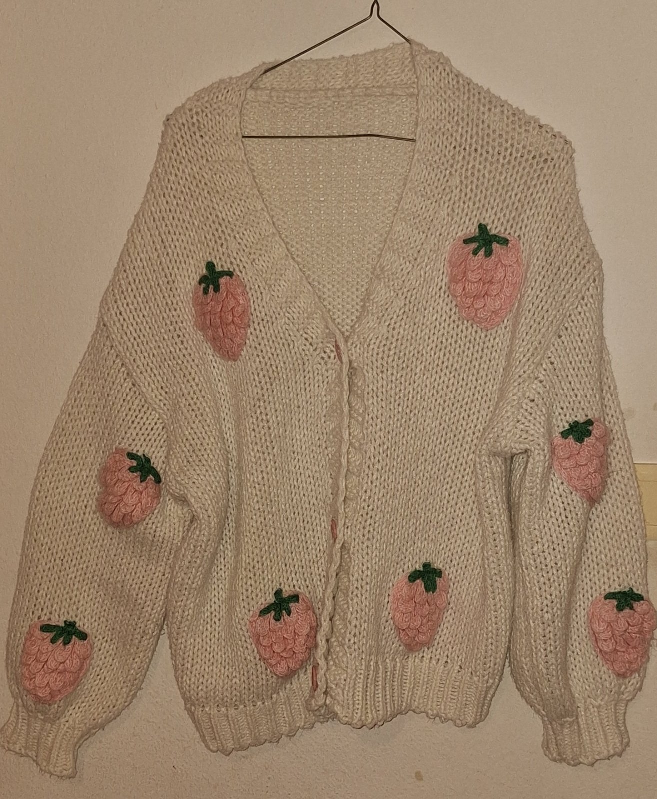 Un cardigan en tricot blanc avec des fraises roses. 
