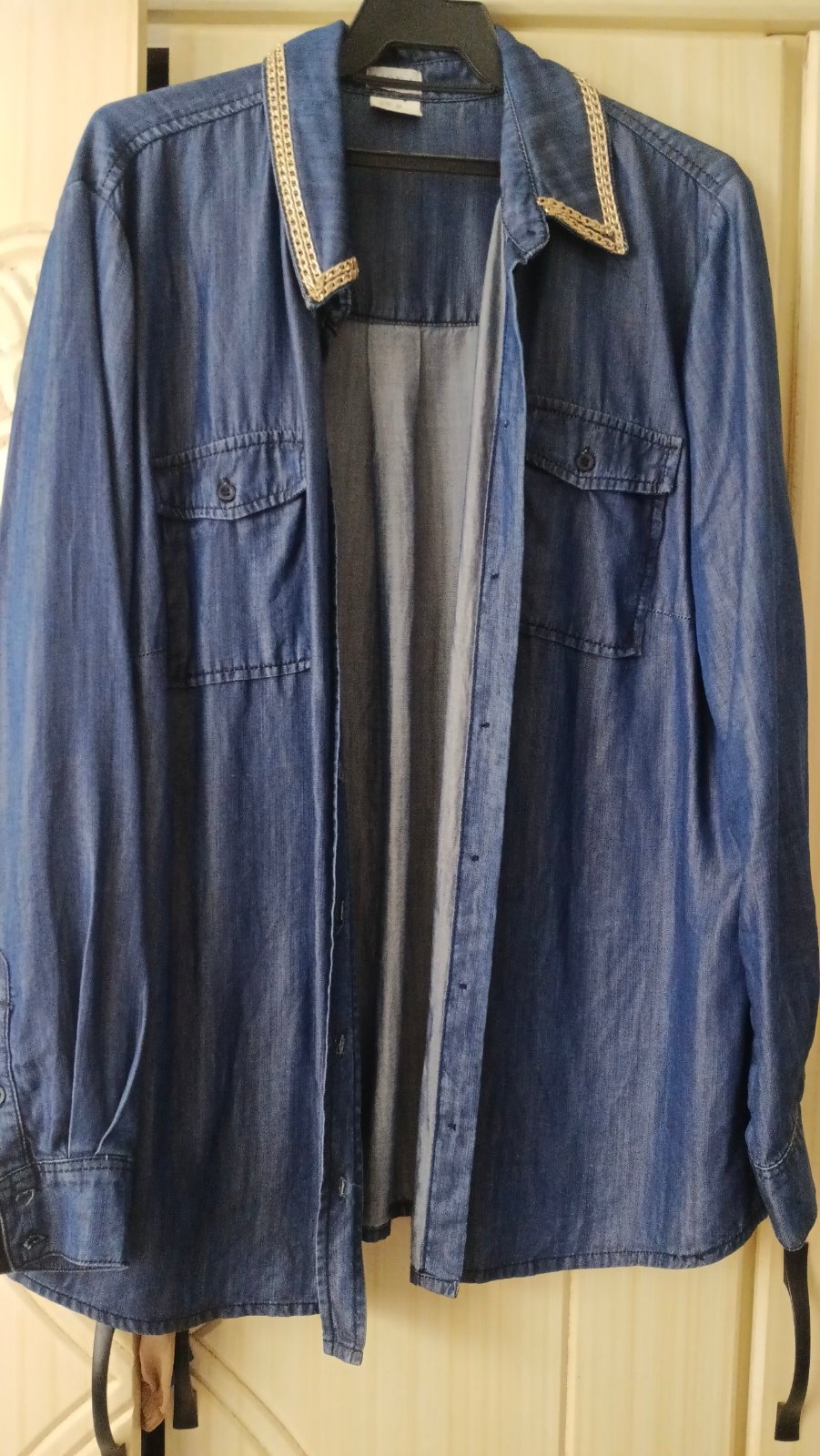 Chemise en jean pour femme présente un délavage bleu moyen, des manches longues et deux poches plaquées sur la poitrine, agrémentée d'un col orné de détails dorés.