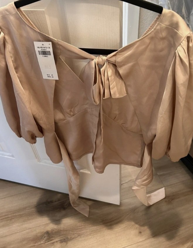 Un chemisier satiné de couleur champagne avec des manches bouffantes et une fermeture boutonnée à l'avant 
