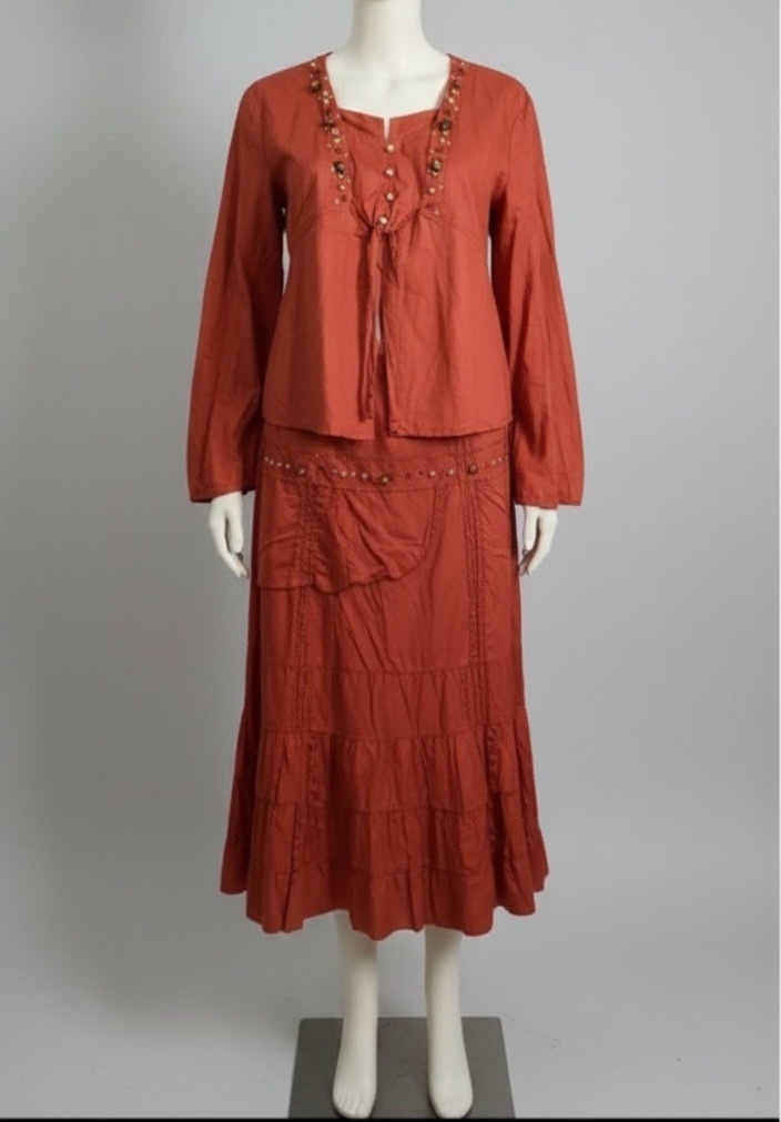 Ensemble deux pièces porter 42/46 en tissu léger terracotta. Haut à manches longues avec col tunisien, laçage et détails artisanaux (perles, boutons, pierres). Jupe longue, fluide et légèrement froncée pour un joli tombé bohème.
