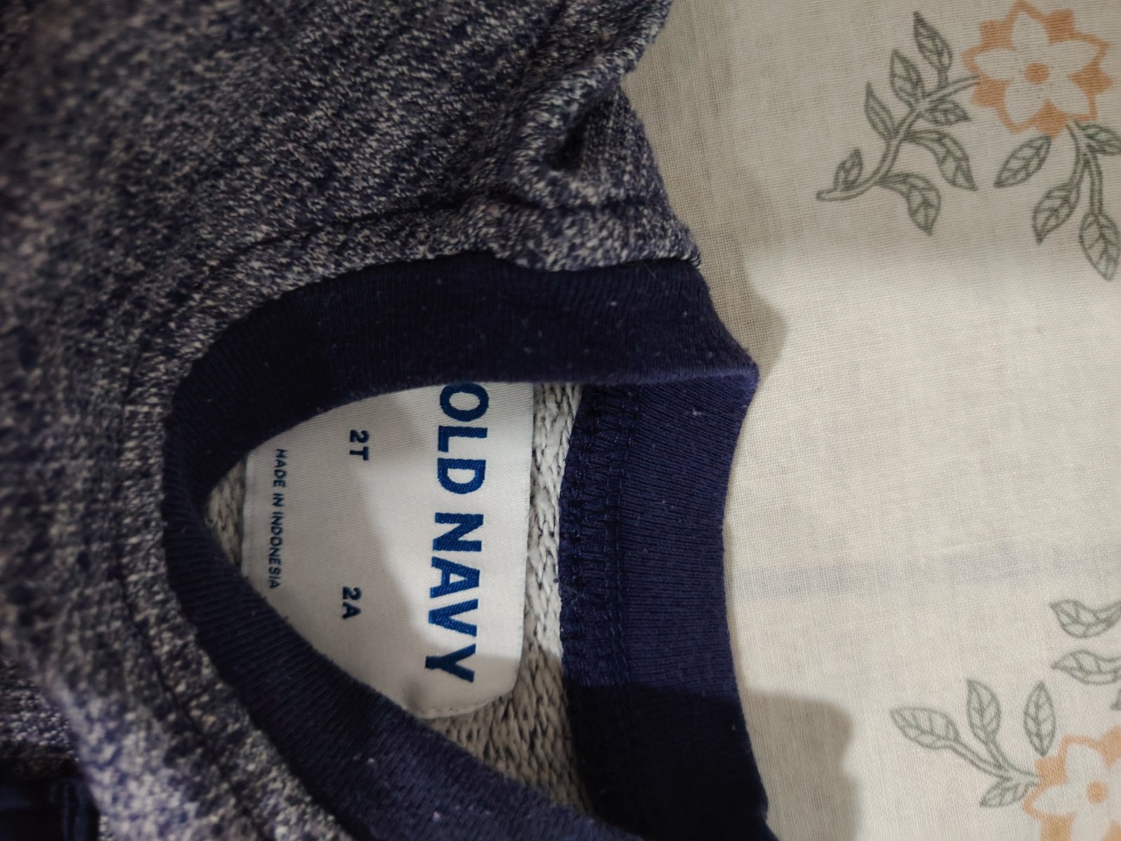 Un pull ou sweat-shirt à manches longues de couleur bleu chiné (mélangé), doté d'un col rond et d'une poche poitrine contrastée bleu marine avec un bouton-pression