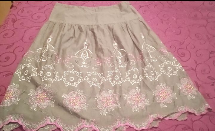 Une jupe trapèze gris-vert avec des broderies florales blanches et roses sur le bas et un ourlet festonné rose