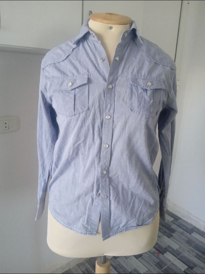 Une chemise western boutonnée de couleur bleu clair avec des poches à rabat et des boutons-pression. 