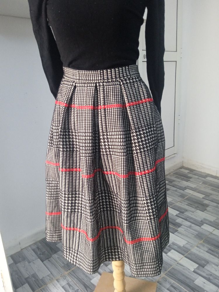 Une jupe taille haute midi plissée à motif pied-de-poule noir et blanc avec des rayures rouges.