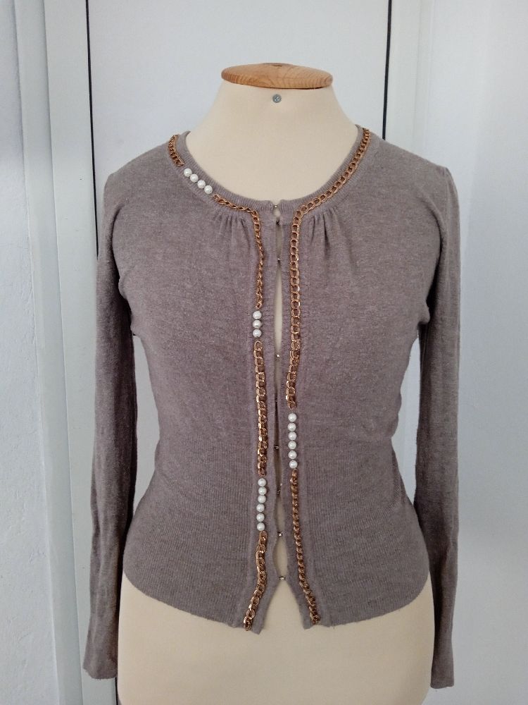 Un cardigan marron taupe pour femme avec des chaînes dorées et des perles décoratives le long de l'ouverture et de l'encolure.