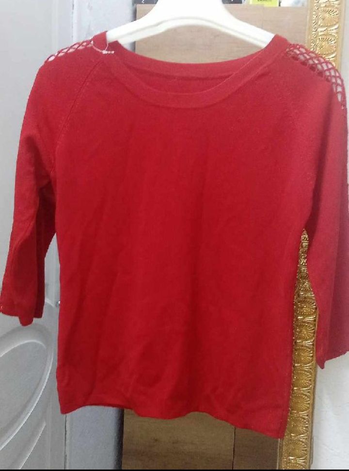 Un pull court rouge vif à manches trois-quarts avec des détails en crochet sur les épaules.