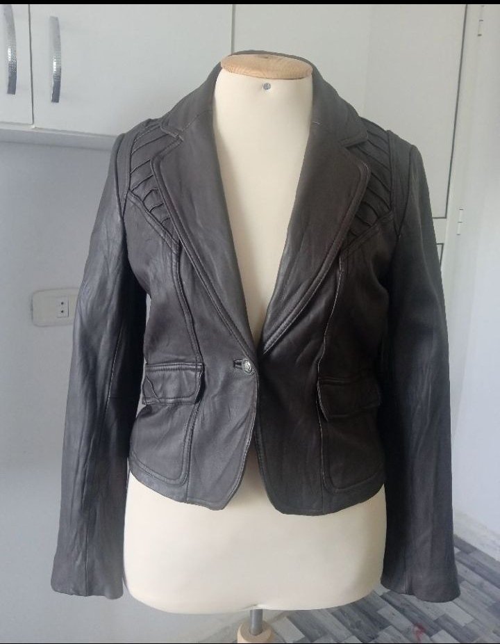 Une veste blazer en cuir marron foncé avec des détails plissés sur les épaules et des poches à rabat.
