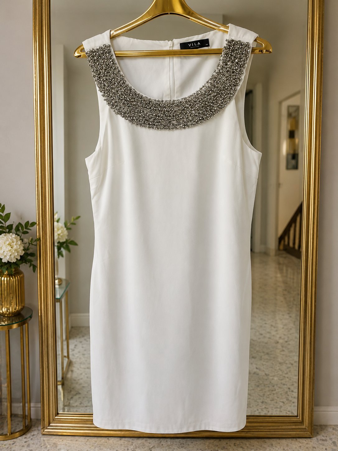 Très jolie robe droite Vila de couleur blanc cassé.Sans manches, longueur au dessus des geoux, encolure dotée de perles et sequins gris argenté. Avec doublure. Fermeture zippée au dos. 