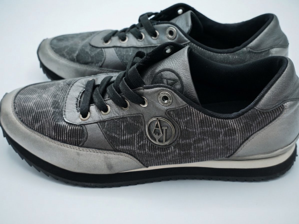         Il s'agit d'une paire de baskets Armani Jeans grises et argentées dotée d'un logo AJ circulaire distinctif sur le côté.        Il s'agit d'une paire de baskets Armani Jeans grises et argentées dotée d'un logo AJ circulaire distinctif sur le côté.
