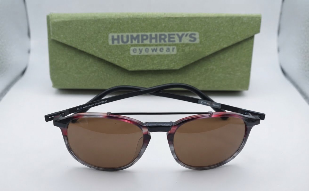 Lunettes avec des branches noires  original et un contour de verres aux tons rouge et gris/marron (faisant penser à une monture de la marque Dilem fabriquée en France, modèle de type pantos avec double pont),