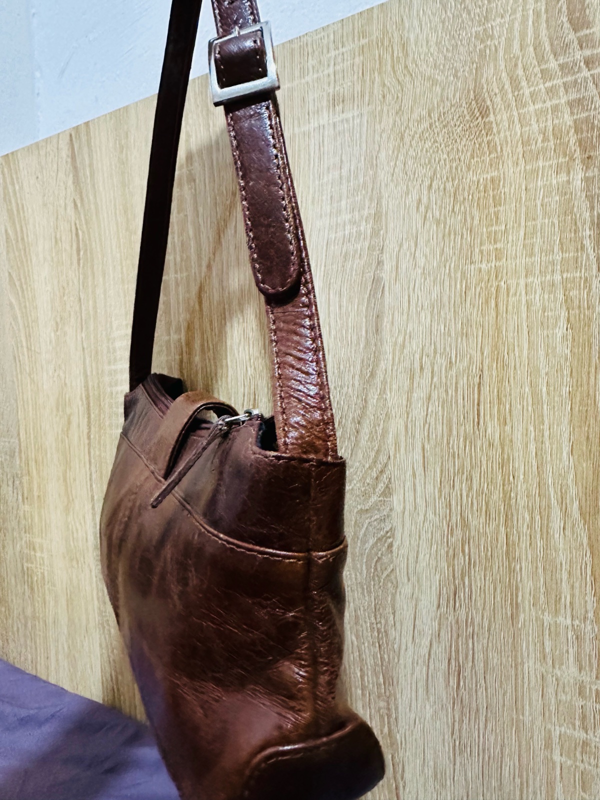 Ce sac à bandoulière marron en cuir vintage, rappelant le style "moto" ou "Y2K", est doté d'une sangle distinctive avec trois œillets métalliques