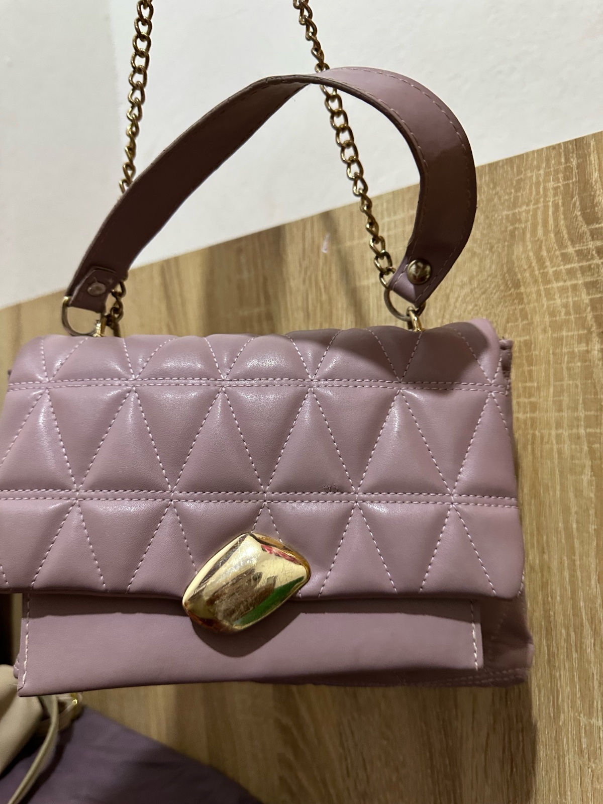 Ce sac à main en cuir synthétique de couleur lilas est doté d'un matelassage géométrique et d'un fermoir métallique doré.
