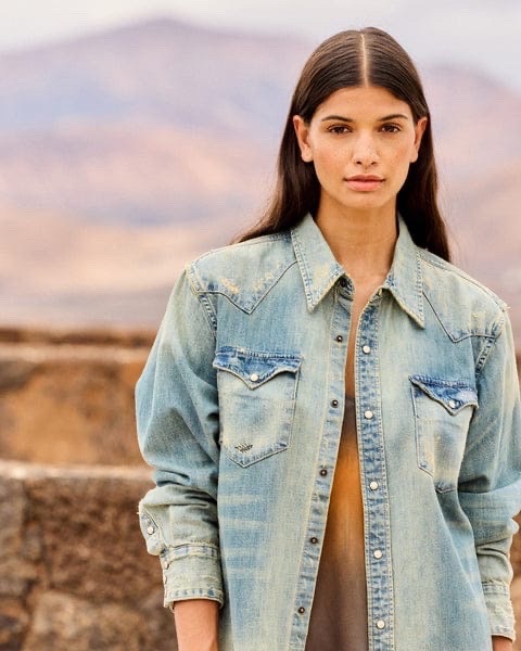Chemise est un modèle en jean de la marque Mango, caractérisé par une décoloration claire et une coupe de style western avec des poches poitrine à rabat.
