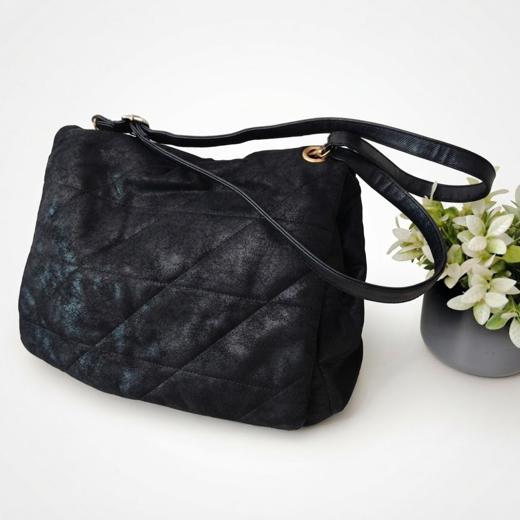 Grand sac à main noir matelassé de la marque C&A. Il s'agit d'un modèle d'épaule doté d'un fini effet velours ou suède noir avec des surpiqûres en diagonales formant un motif géométrique élégant. Largeur 35cm