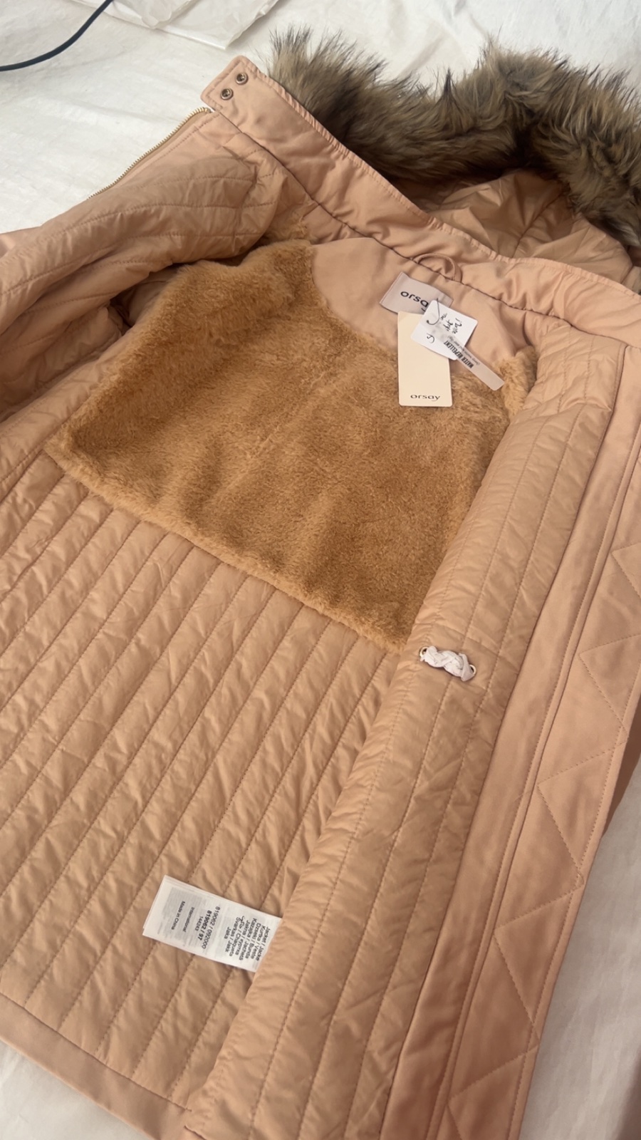 Veste d'hiver de la marque Orsay de couleur beige/rose nude, dotée d'une fermeture éclair dorée centrale, de deux poches obliques zippées sur le devant et d'une capuche bordée de fausse fourrure amovible.