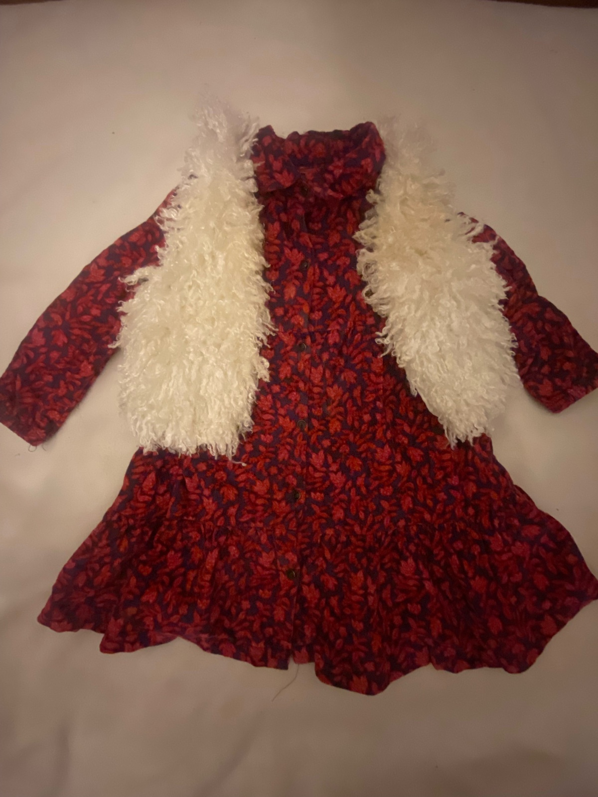 D'une robe enfantine à motif floral rouge avec un gilet en fausse fourrure blanche