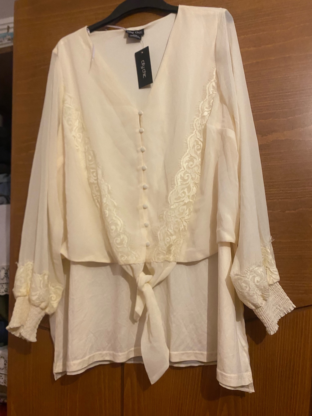 Un chemisier blanc cassé de la marque City Chic avec des détails en dentelle et des manches longues.
