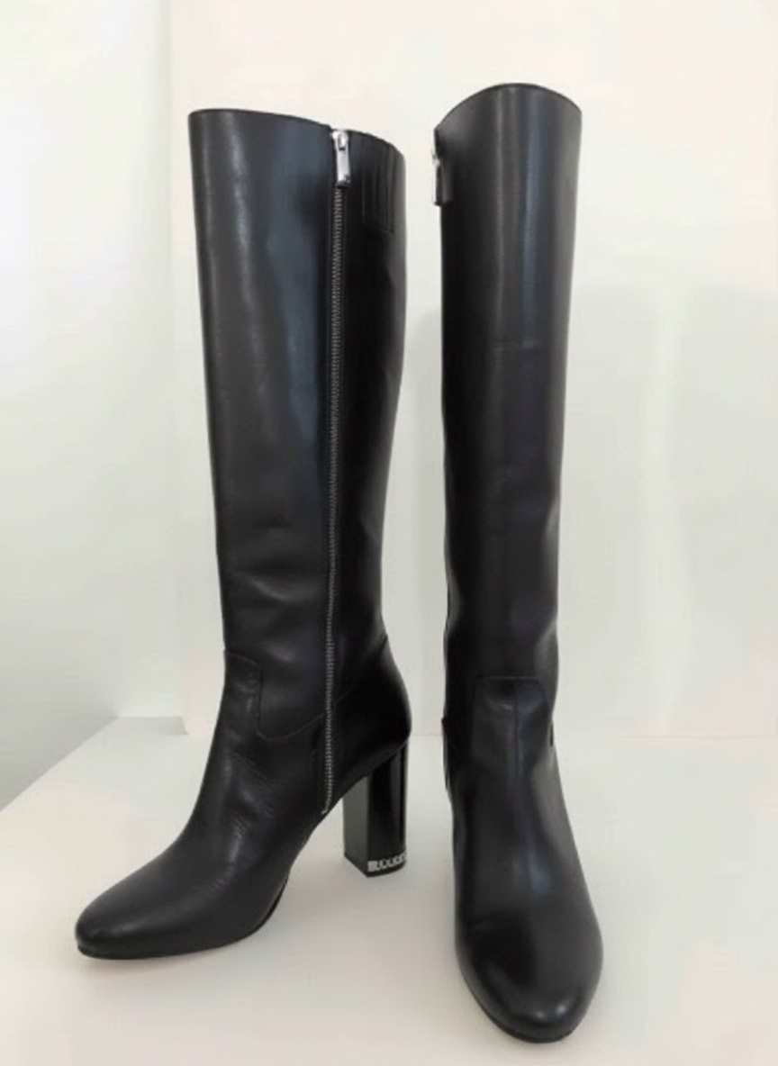 Bottes au genou en cuir noir Michael Michael Kors avec talons blocs et chaîne en argent 'MK'.   Fermeture éclair argentée avec logo Michael Kors. 