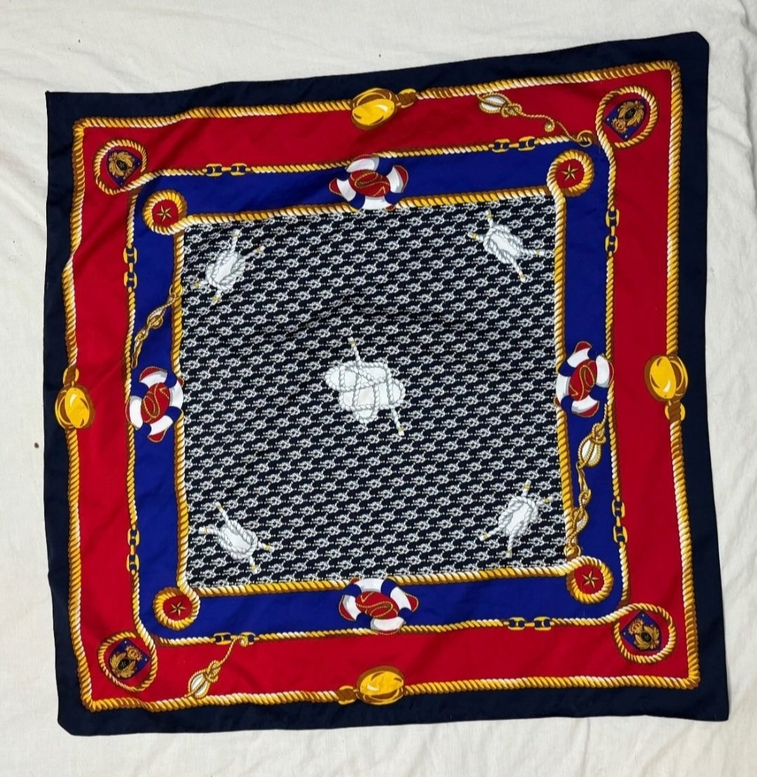 Ce carré de soie vintage Atelier Versace arbore un motif nautique vibrant avec des cordes et des bouées sur un fond rouge, bleu et noir