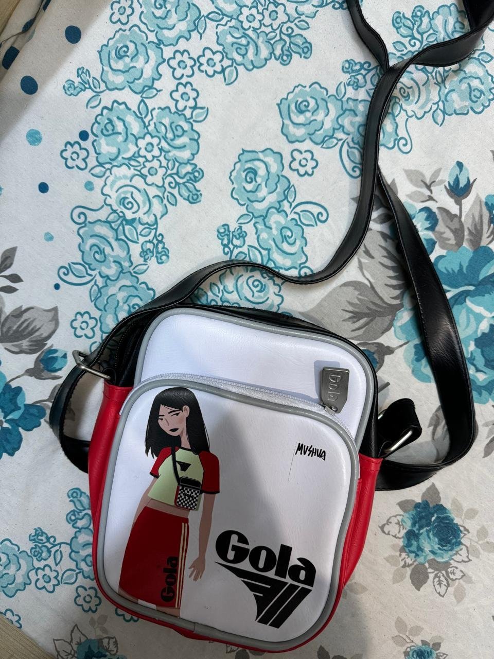 Sac bandoulière Gola présente un design blanc avec des accents rouges et noirs, affichant un graphique de personnage stylisé sur le devant