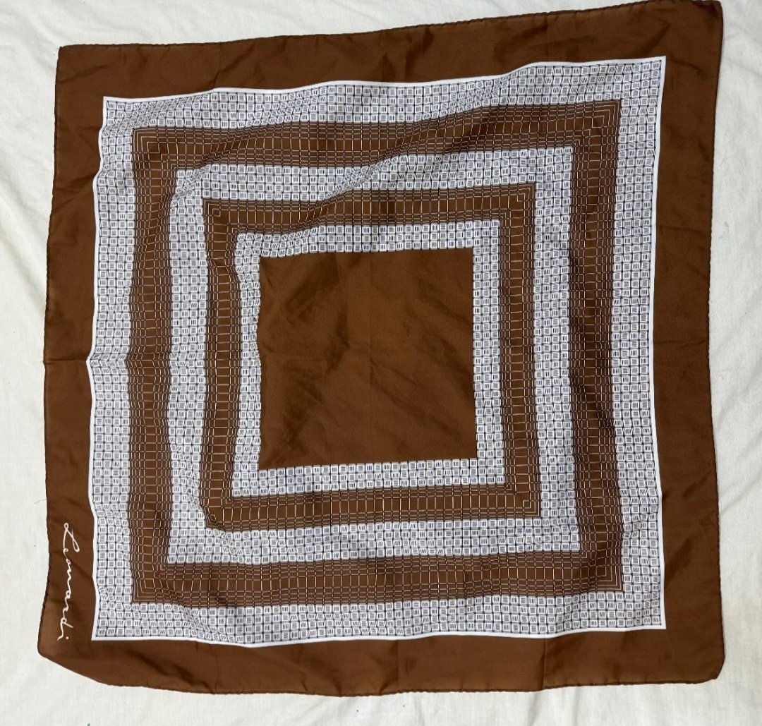 Foulard carré marron arbore des motifs géométriques concentriques blancs et une signature discrète sur le côté