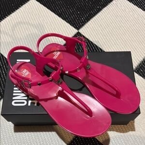 Sandales d'entre-doigts en plastique rose vif sont dotées de brides ornées de petits rivets métalliques et d'une lanière de cheville réglable