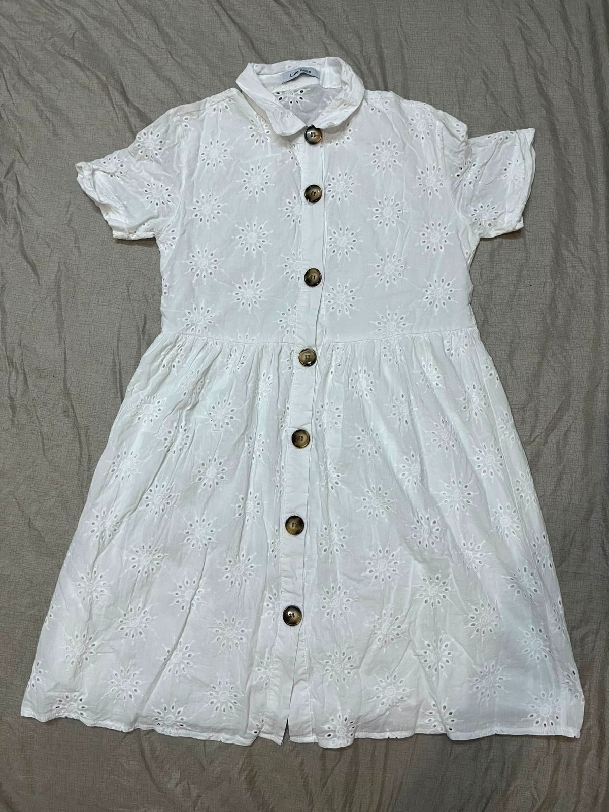 Robe blanche en broderie anglaise présente des boutons marron distinctifs et un col classique