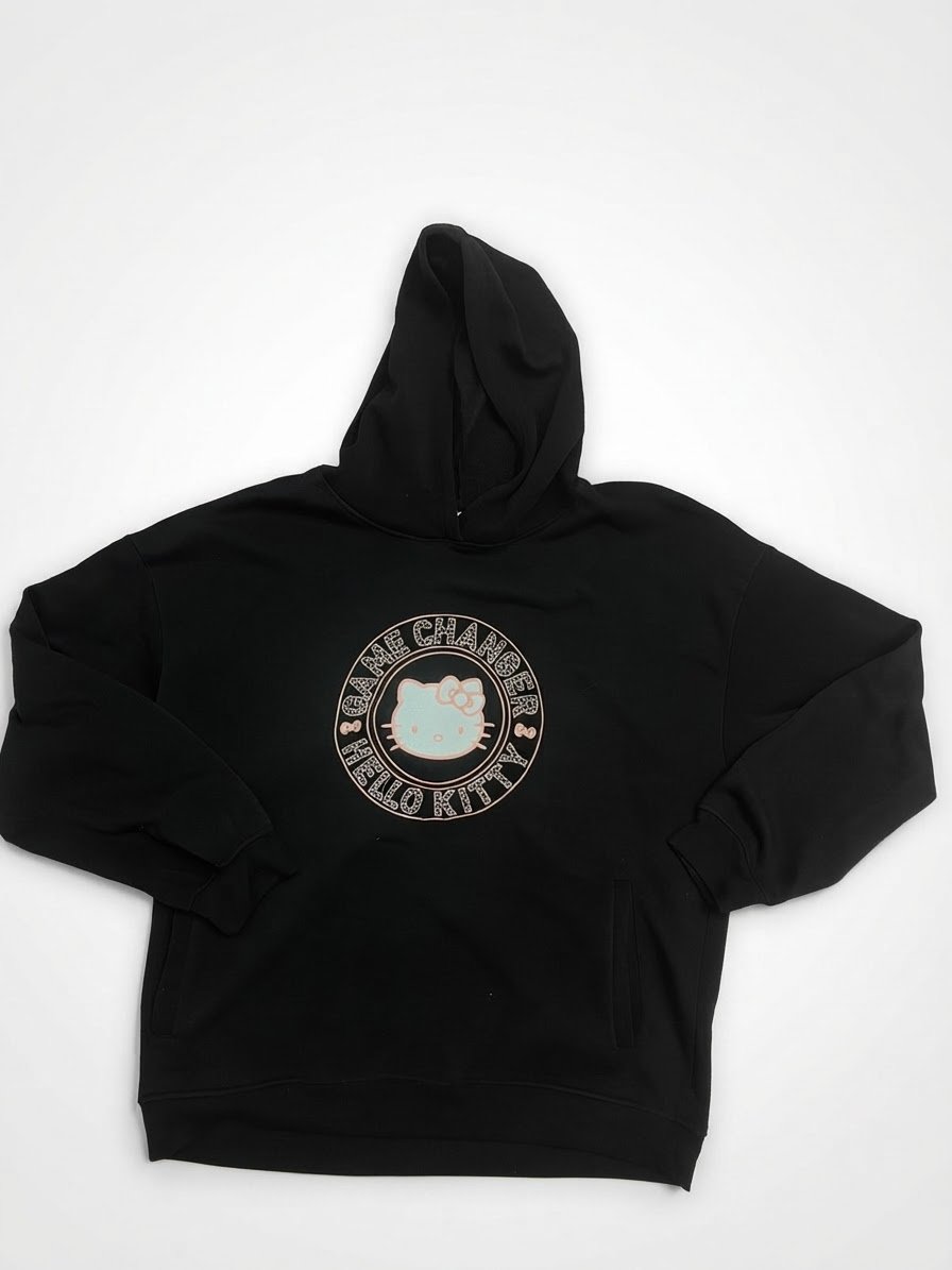Sweat-shirt à capuche (hoodie) noir à manches longues, doté d'une poche kangourou sur le devant et orné d'un motif rond sur la poitrine représentant le personnage Hello Kitty encerclé par l'inscription « HELLO KITTY - GAME CHANGER »