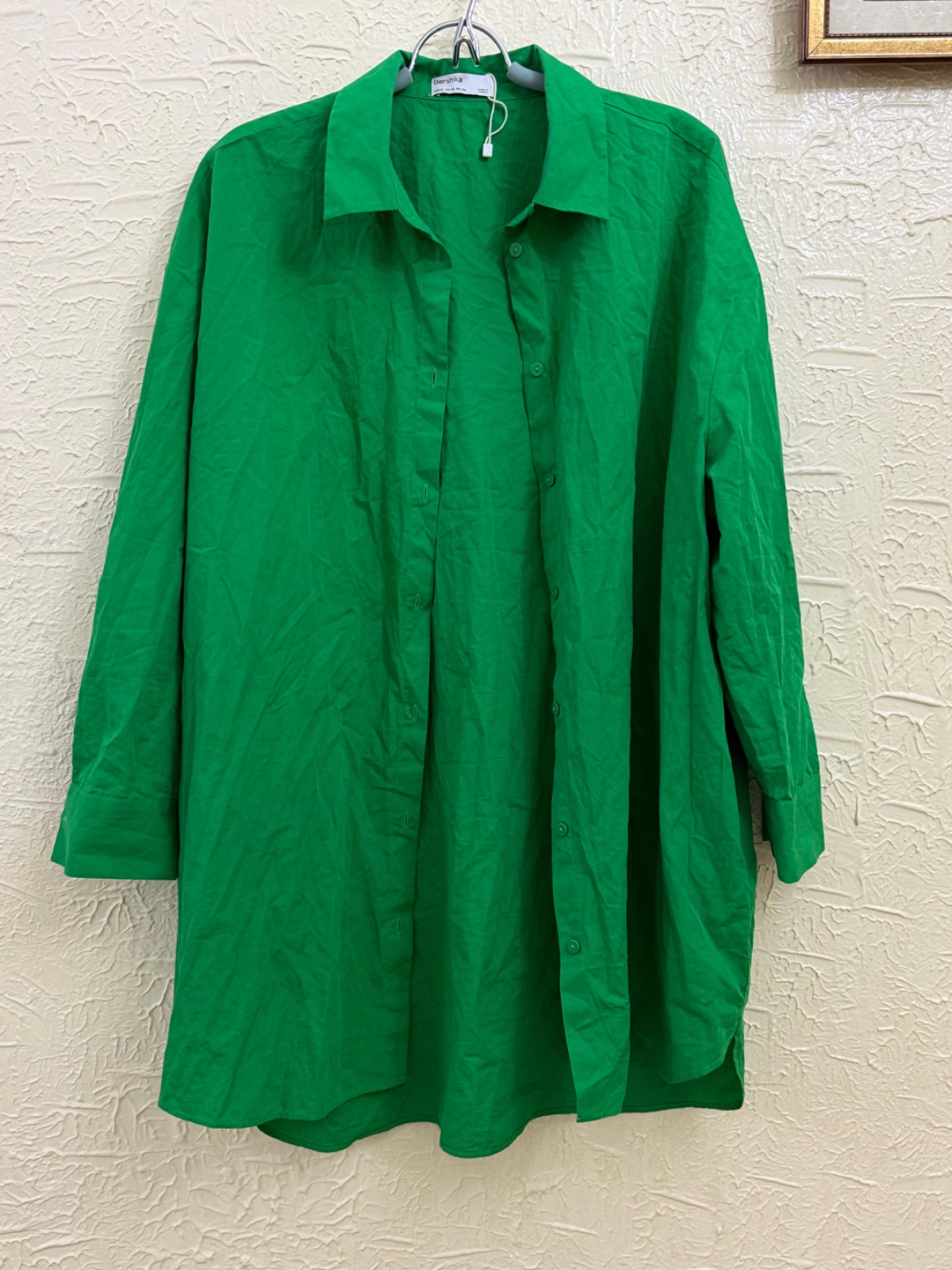 Cette chemise oversize verte est un modèle de la marque Bershka, caractérisé par sa coupe décontractée et sa fermeture entièrement boutonnée