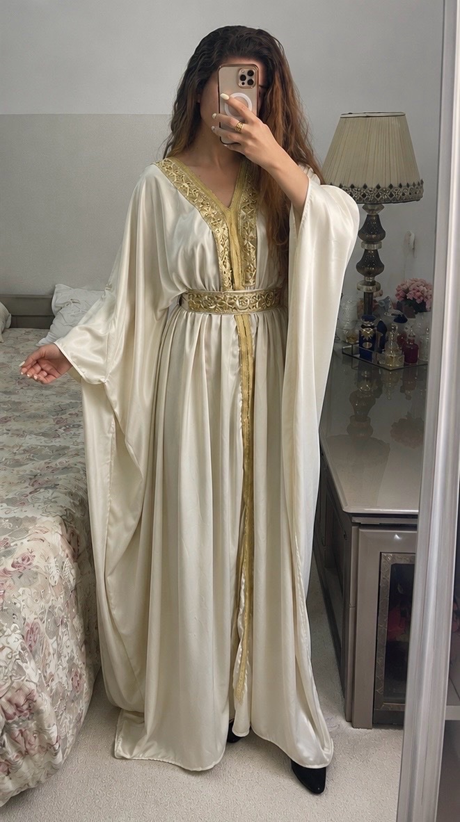 Robe caftan ou jebba de couleur beige/dorée, conçue dans un tissu léger, est ornée de broderies dorées délicates le long du décolleté et de la ceinture ylabes tous les taille 