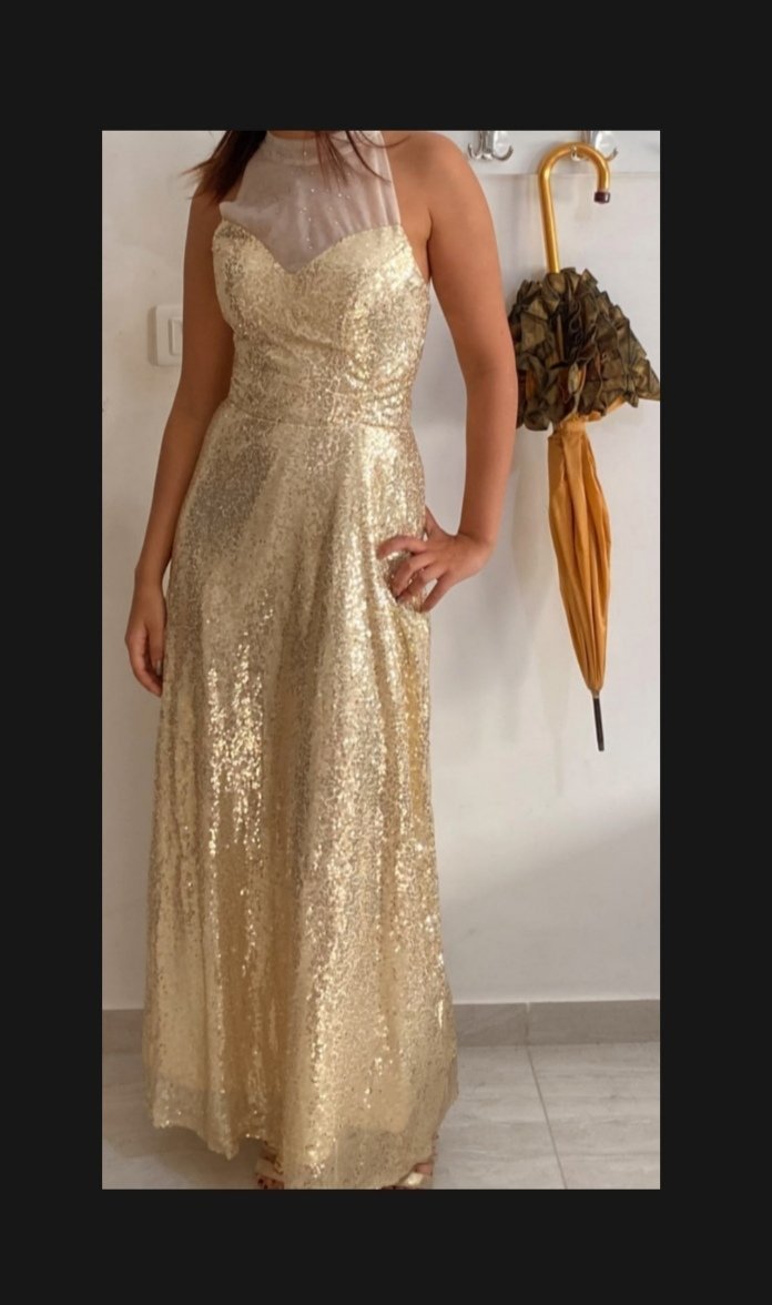 Une longue robe de soirée élégante de couleur dorée, entièrement recouverte de paillettes scintillantes. La robe présente un corsage ajusté avec un décolleté en cœur. 