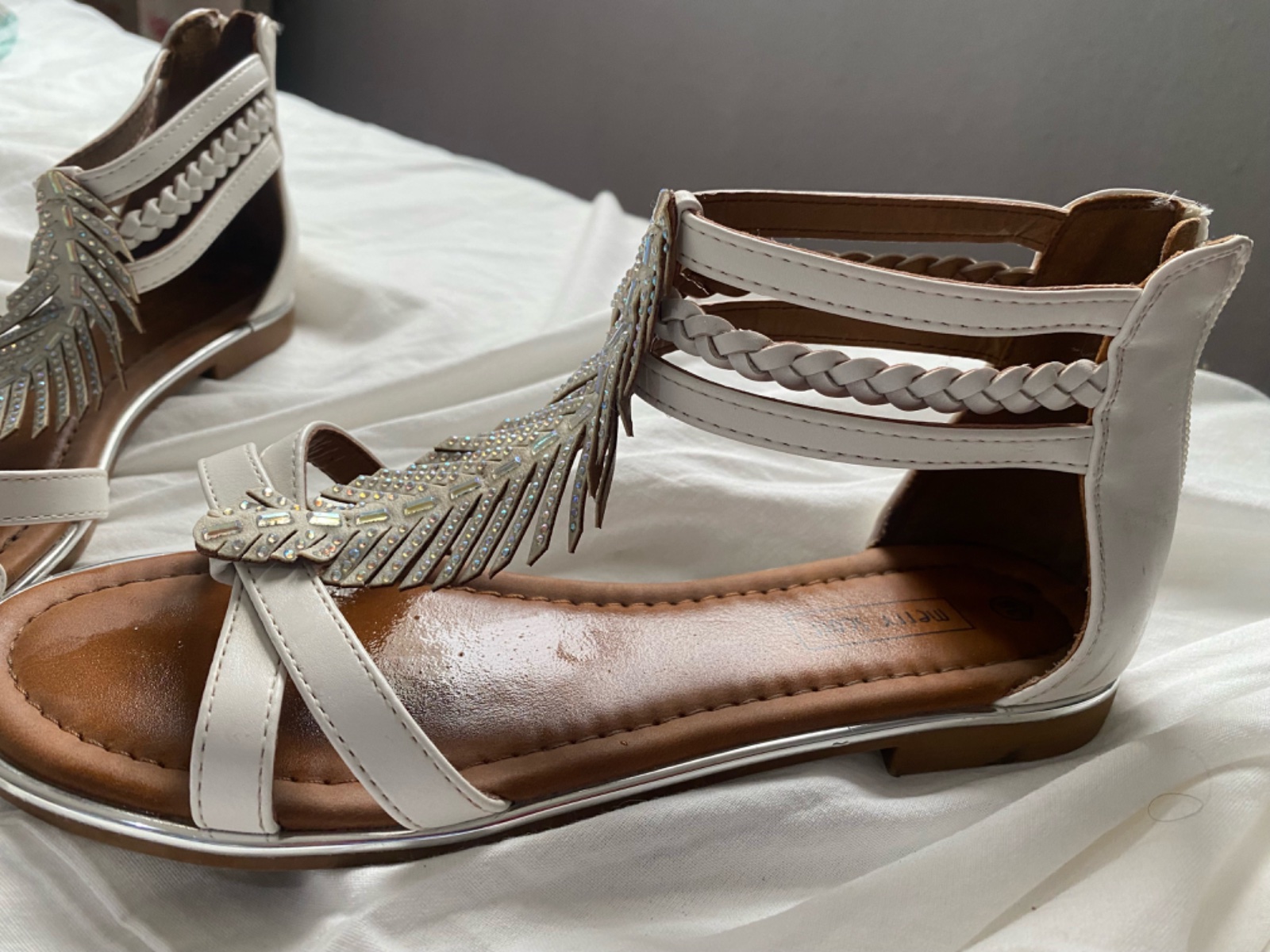 Ce sont des sandales 🇫🇷plates blanches ornées d'un motif de plume brillant de type strass.