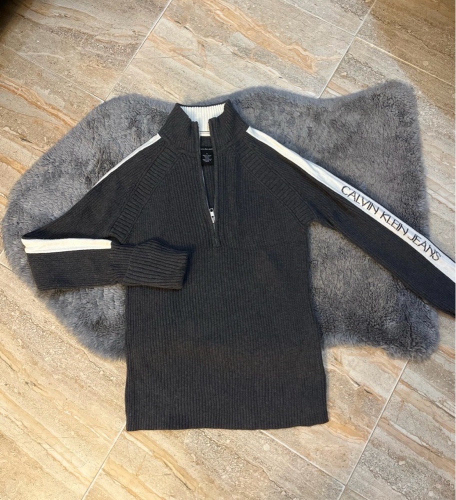 Pull Calvin Klein Jeans en maille gris foncé à fermeture éclair,avec des bandes blanches sur les manches et le logo de la marque sur la manche gauche