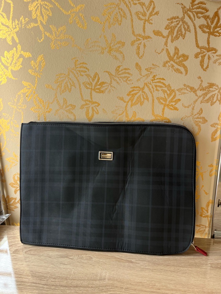  Pochette pour ordinateur portable ou une pochette de la marque Burberry, caractérisée par son motif à carreaux distinctif et son logo en métal sur le devant