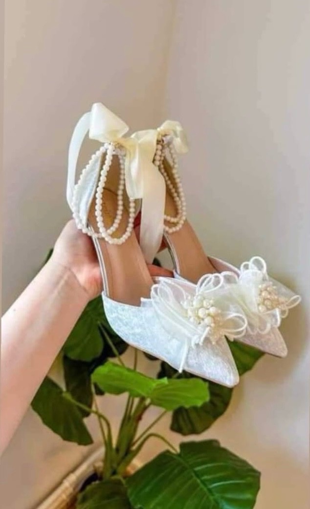 Escarpins de mariée blancs en dentelle ornés de chaînes de perles à la cheville et d'un grand nœud en tulle agrémenté de perles sur le devant