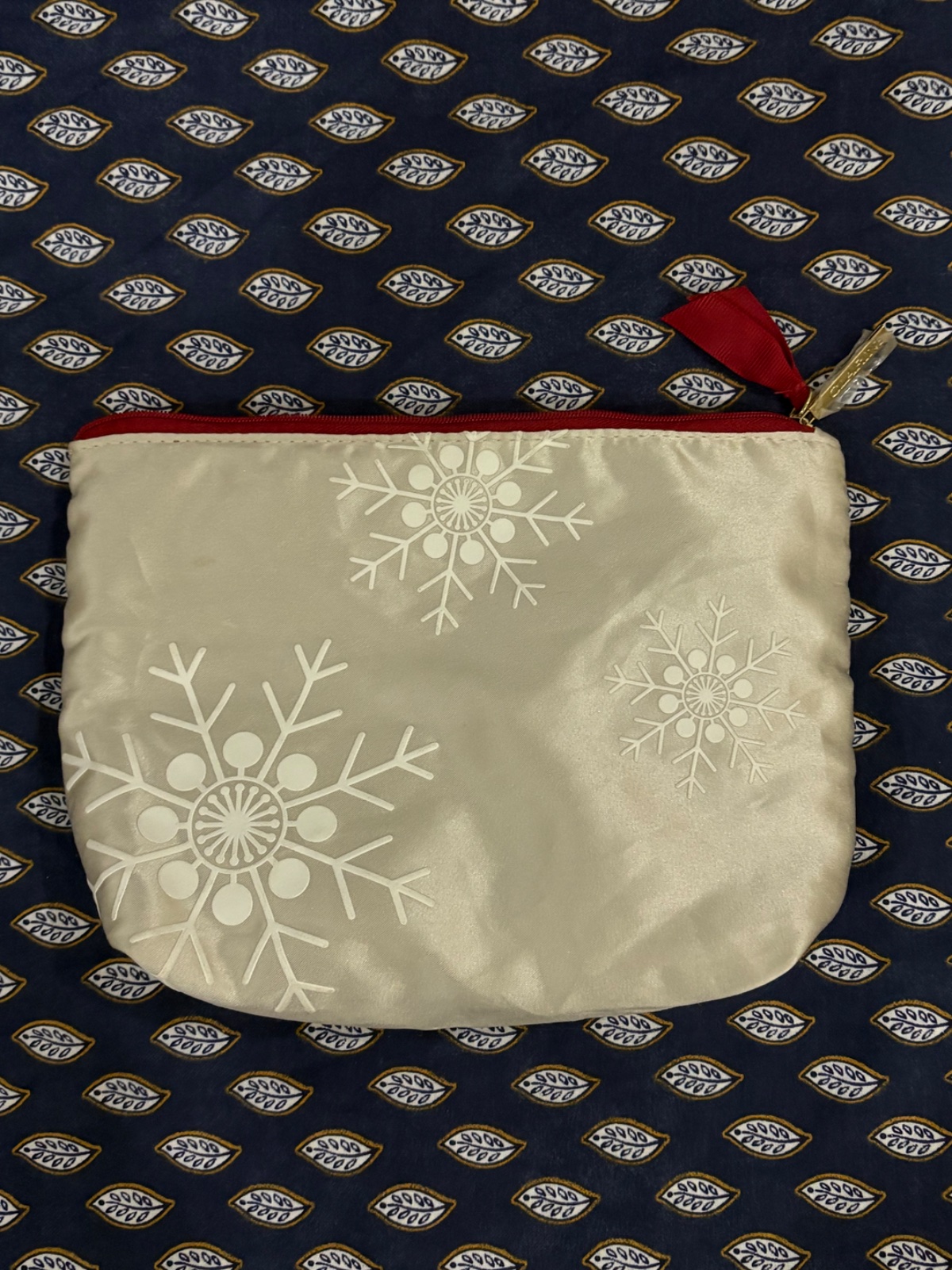 Trousse à maquillage de la marque Clarins ornée de flocons de neige  avec une fermeture éclair rouge