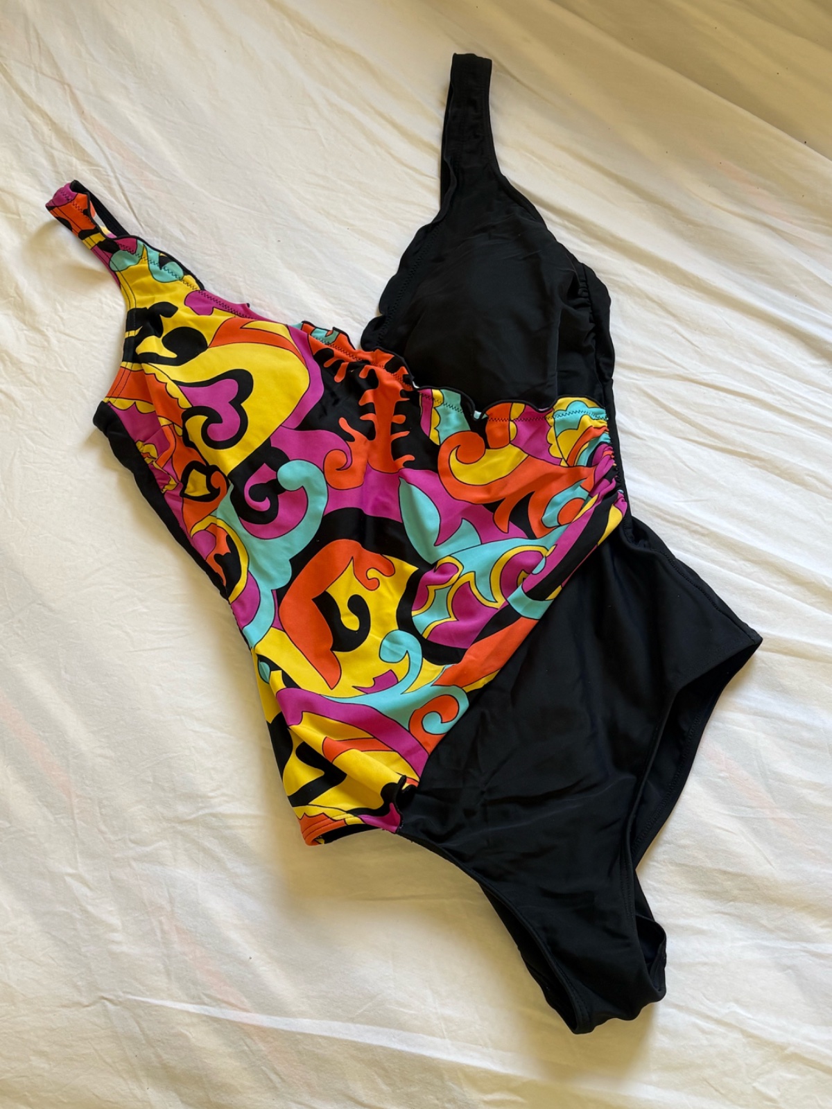 Maillot de bain une pièce présente un design asymétrique avec une bretelle unique et un motif psychédélique multicolore contrastant avec un côté noir uni 