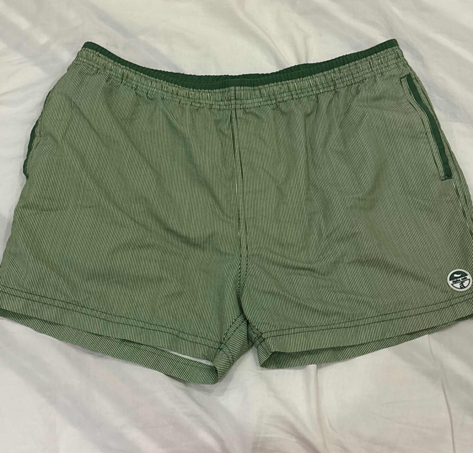 Short de bain vert rayé présente une taille élastique confortable et un petit logo circulaire sur la jambe gauche