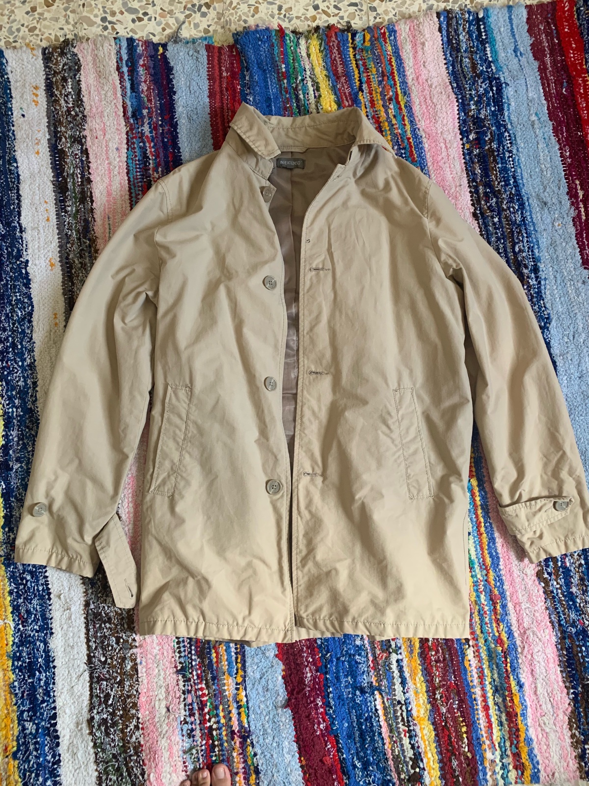 Manteau imperméable beige pour homme doté d'une fermeture boutonnée classique sur le devant.