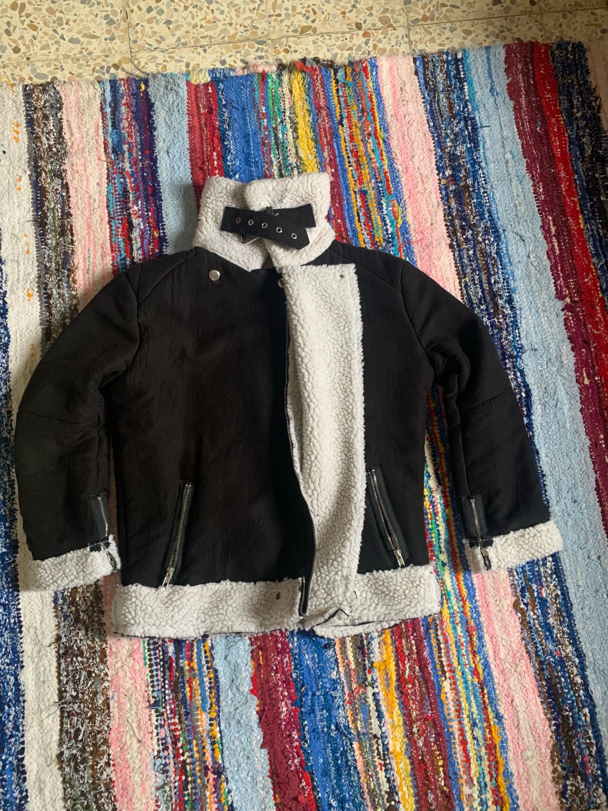 Veste aviateur noire dotée d'une doublure et d'un col en fausse fourrure blanche contrastante.