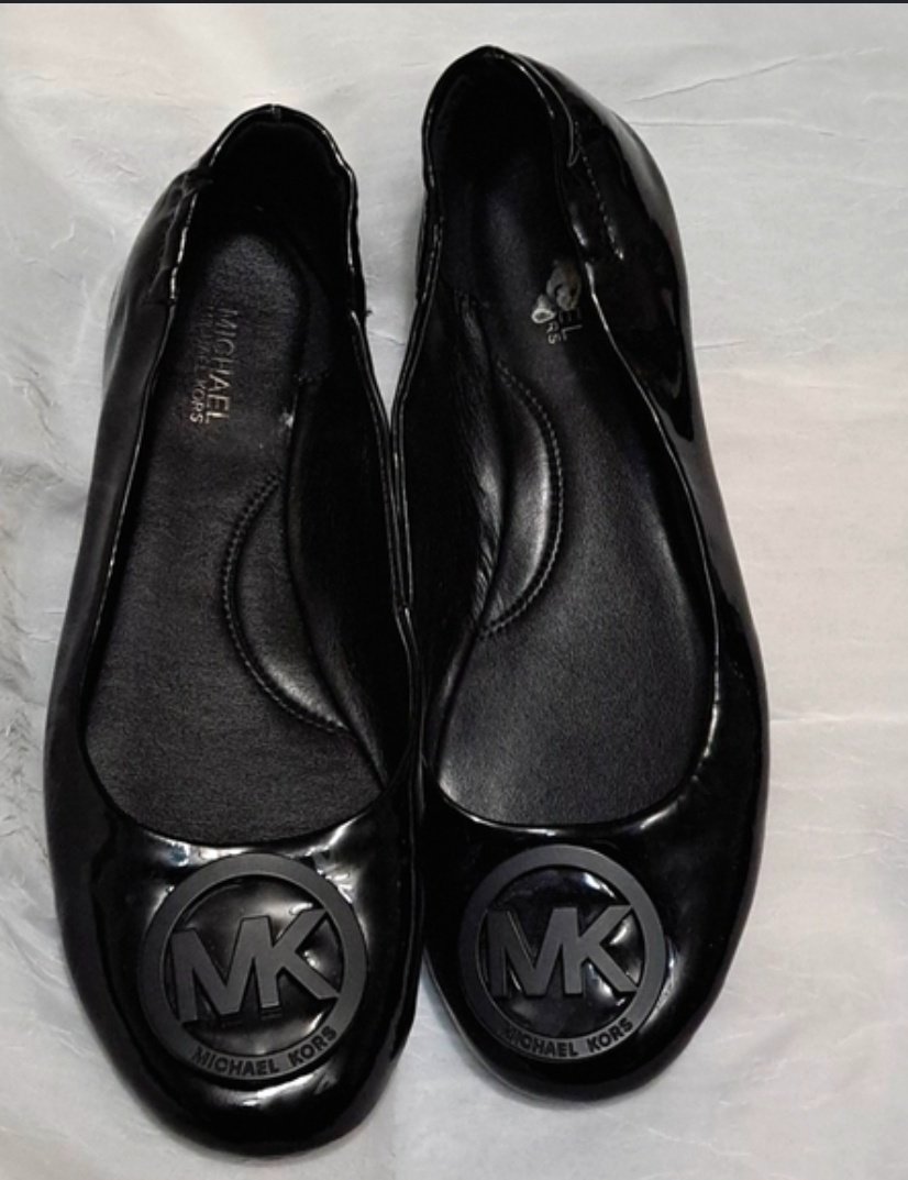 Ces ballerines plates noires en cuir verni de la marque Michael Kors arborent un bout rond et un médaillon distinctif ton sur ton gravé du logo « MK » sur l'avant.