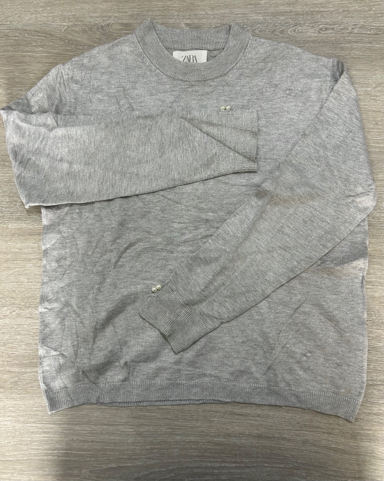 Pull gris à manches longues de la marque Zara, orné de petits détails de perles sur les poignets et près de l'encolure