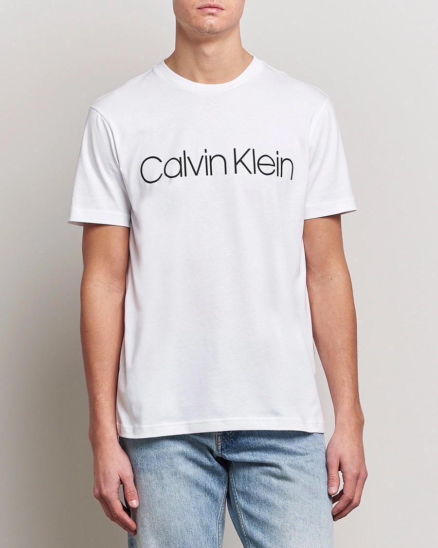 Ce t-shirt blanc Calvin Klein arbore un logo noir imprimé sur la poitrine et présente un col rond classique