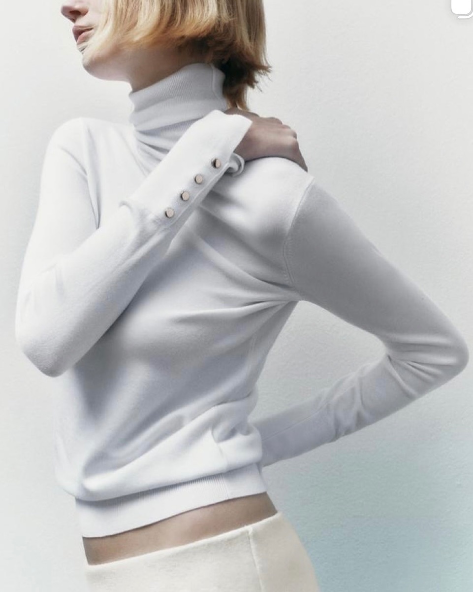 Pull fin à col roulé et à manches longues de couleur blanche ou écru, agrémenté de petits boutons décoratifs aux poignets